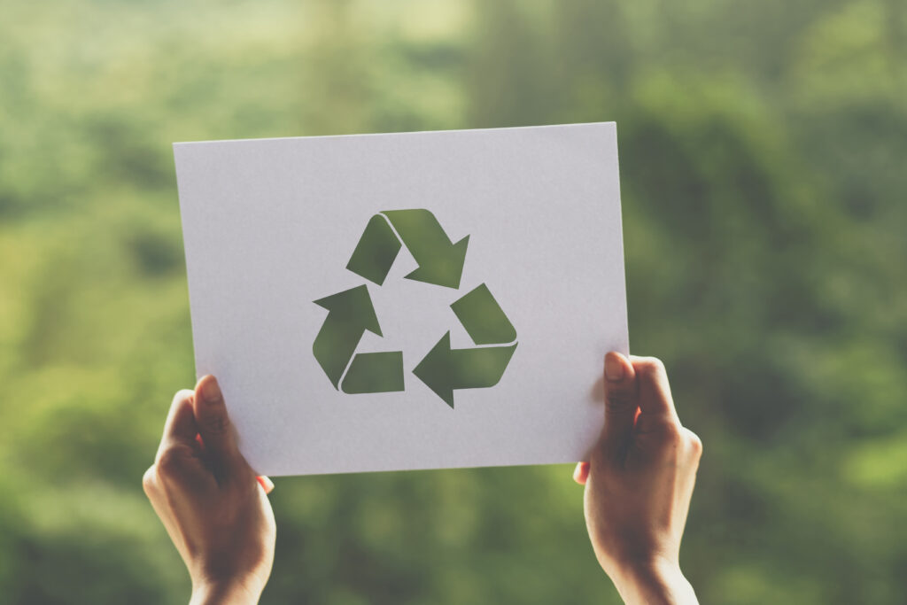 Manos sosteniendo un cartel con el símbolo del reciclaje sobre un fondo natural